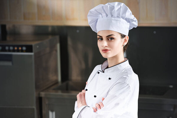 Professional female chef standing with arms folded on modern kitchen