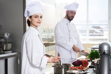 Professional chefs working by stove on modern kitchen clipart