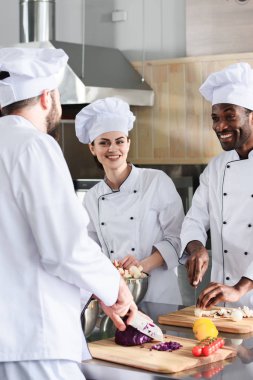 Multiracial chefs team smiling and cooking on modern kitchen clipart