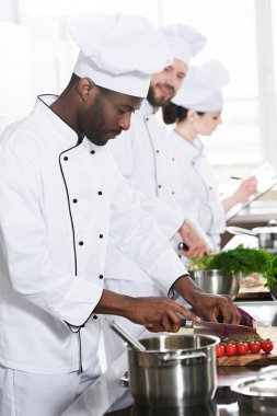 Multiracial chefs team cutting ingredients by kitchen table clipart