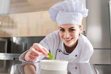 Female chef garnishing dish on restaurant kitchen clipart