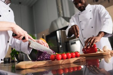 Multiracial chefs team cutting raw vegetables in kitchen clipart