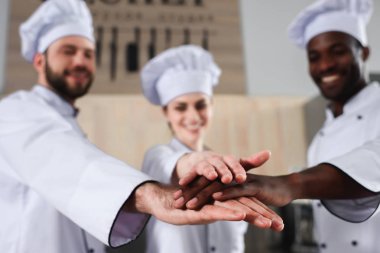 Multiracial tram of cooks stacking hands together on modern kitchen clipart