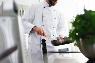 cropped image of chef frying food on frying pan at restaurant kitchen clipart