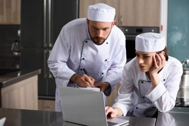 male and female chefs using laptop at restaurant kitchen clipart