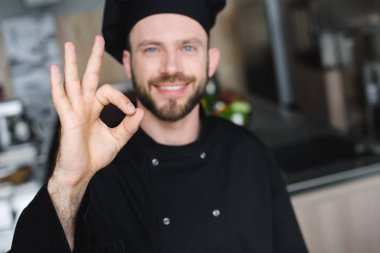 smiling handsome chef showing okay gesture at restaurant kitchen clipart