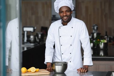 handsome african american chef standing near kitchen counter at restaurant kitchen clipart