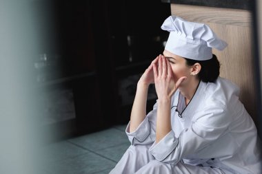 side view of chef crying and sitting on floor at restaurant kitchen clipart