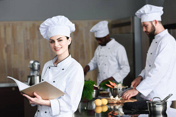 Female chef checking recipe in book by her multiracial colleagues