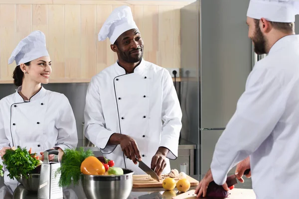 Multiracial team of cooks cutting vegetables on kitchen table