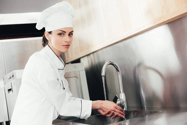 Женщина-повар моет руки над кухонной раковиной
