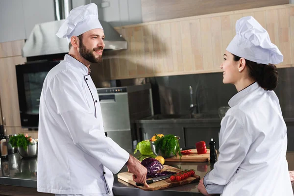 Professional team of cooks sharing sharing experience while cooking on modern kitchen