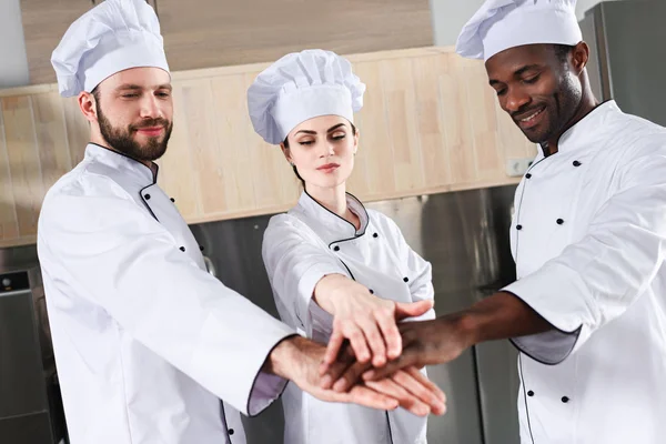 Multiracial chefs team stacking hands together on modern kitchen