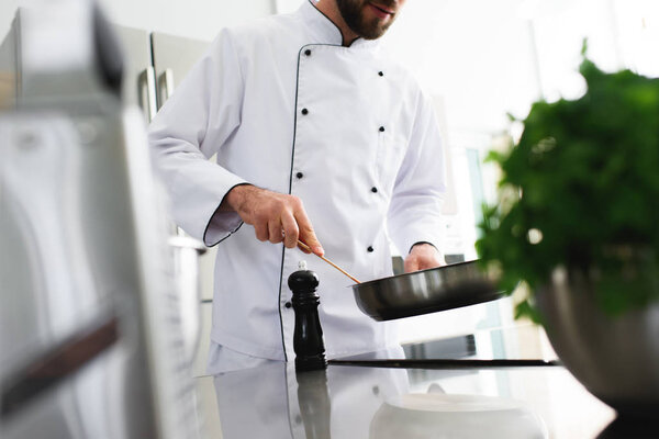 обрезанный образ шеф-повара, жарящего еду на сковородке на кухне ресторана
