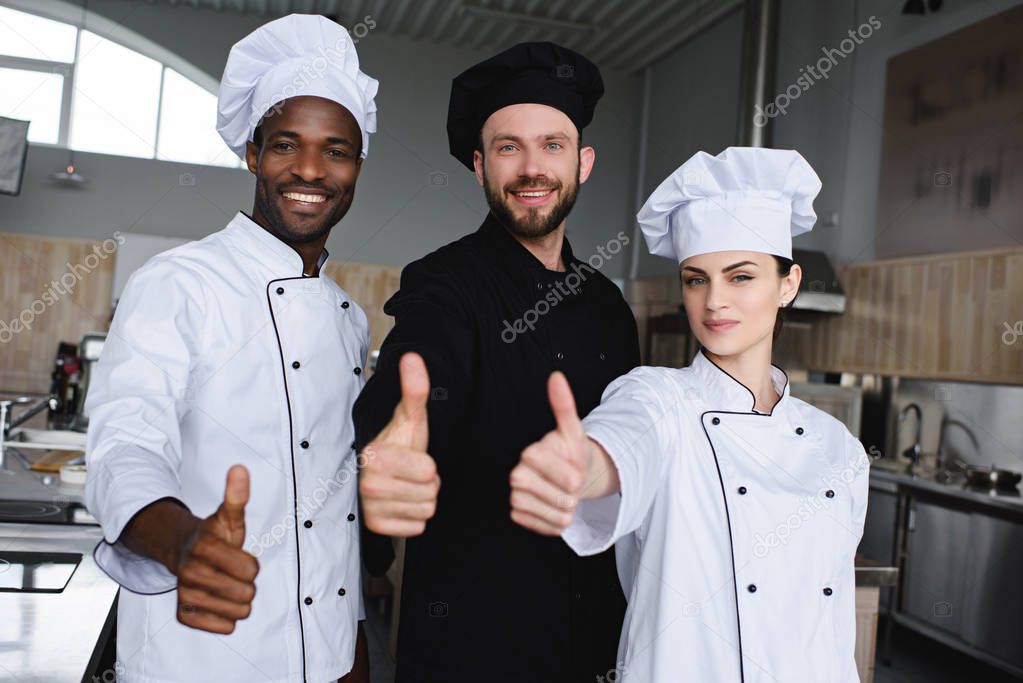 smiling multicultural chefs showing thumbs up at restaurant kitchen