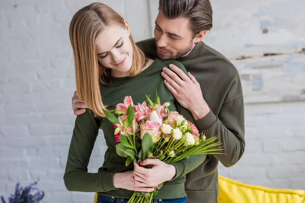 Smiling Man Embracing Young Girlfriend Flowers — Stock Photo, Image