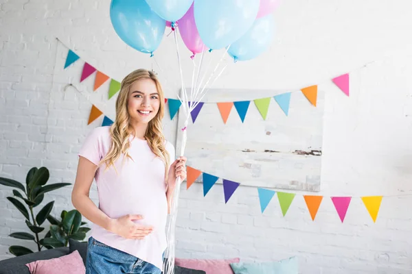 beautiful pregnant woman touching belly and holding bundle of balloons at baby-party