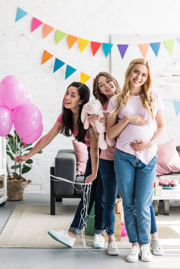 happy multicultural friends and pregnant woman posing with rabbit toy at baby shower party