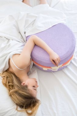 güzel kızın büyük mor macaron yatakta yatıyor Üstten Görünüm