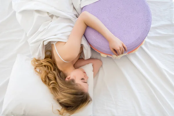top view of blonde woman sleeping with big purple macaron on bed