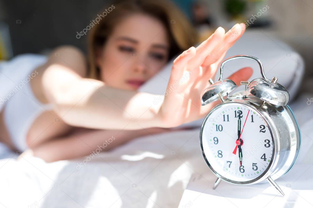 selective focus of woman turning off alarm clock in morning