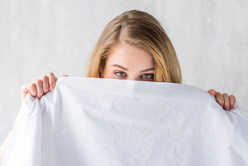 beautiful blonde girl hiding by white sheets