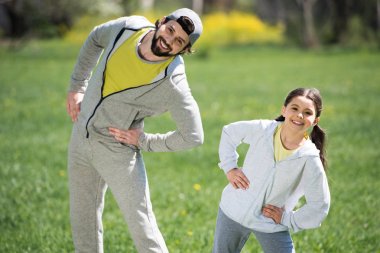 smiling father and daughter doing physical exercise in park clipart