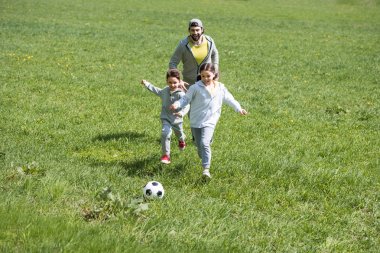Baba ile kızı ve oğlu parkta futbol oynarken