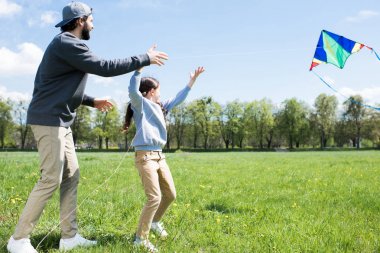 side view of daughter and father flying kite on meadow  clipart