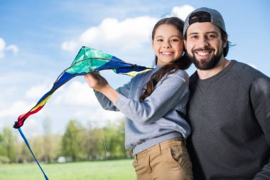 smiling father and daughter holding kite in park clipart