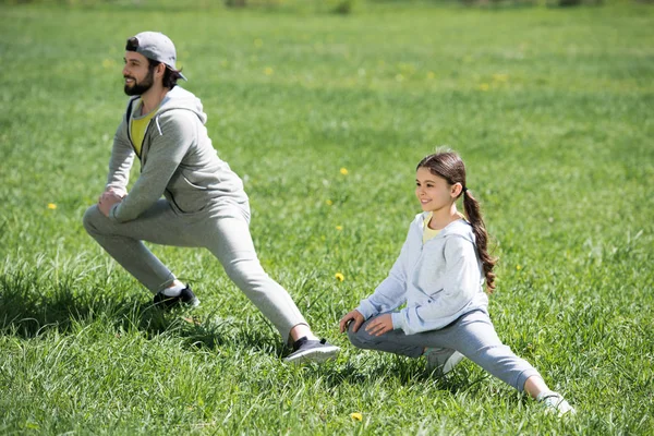 daughter and father doing physical exercise on grass
