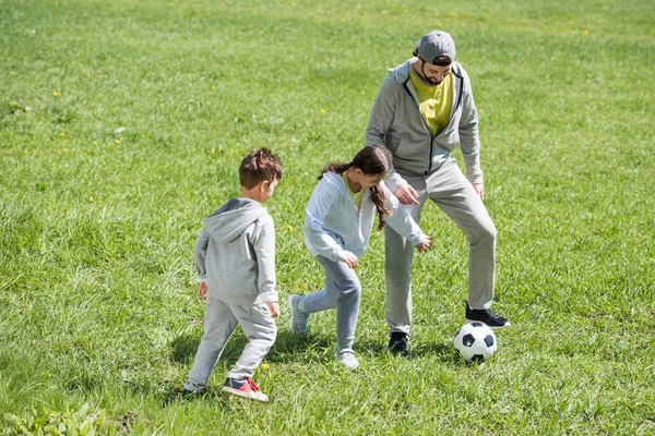 微笑的父亲踢足球与女儿和儿子在公园里 — 图库照片
