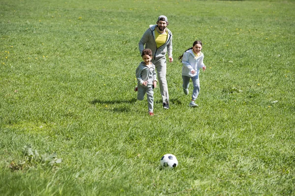 happy sportive family playing football on grassy meadow