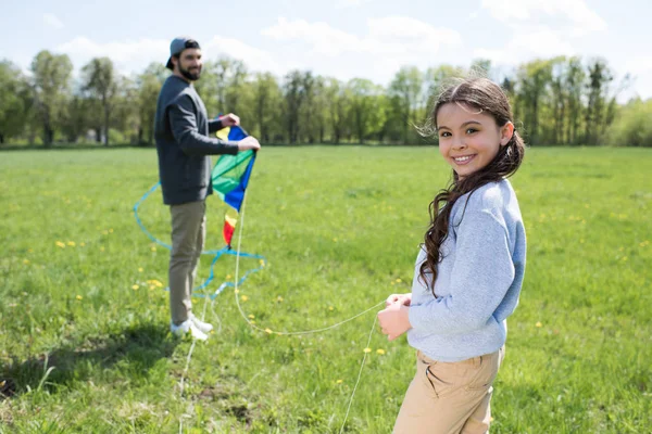 Putri Tersenyum Memegang Layang Layang Dengan Ayah Padang Rumput — Foto Stok Gratis