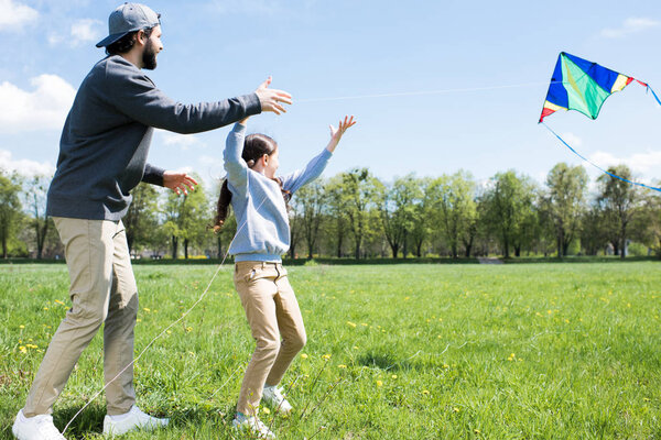 side view of daughter and father flying kite on meadow 