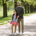 Sonriente padre e hija sosteniendo monopatín en el parque