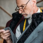 Ernstige volwassen kleermaker met meetlint jasje op etalagepop op naaien workshop onderzoeken