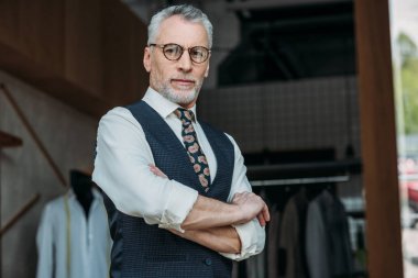 çapraz kolları ile ayakta ve Dikiş Atölyesi kameraya bakarak yakışıklı üst düzey terzi