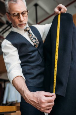 senior tailor measuring sleeve of jacket with tape measure at sewing workshop clipart
