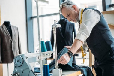 handsome tailor looking at cloth at sewing workshop clipart