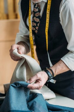 cropped image of tailor choosing cloth at sewing workshop clipart