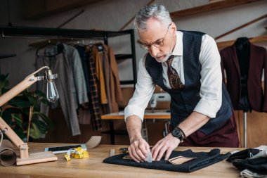 stylish tailor marking cloth pattern with chalk at sewing workshop clipart