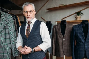 handsome mature tailor looking at camera in sewing workshop clipart