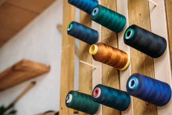 цветные катушки резьбы висят на деревянной стене в швейной мастерской
