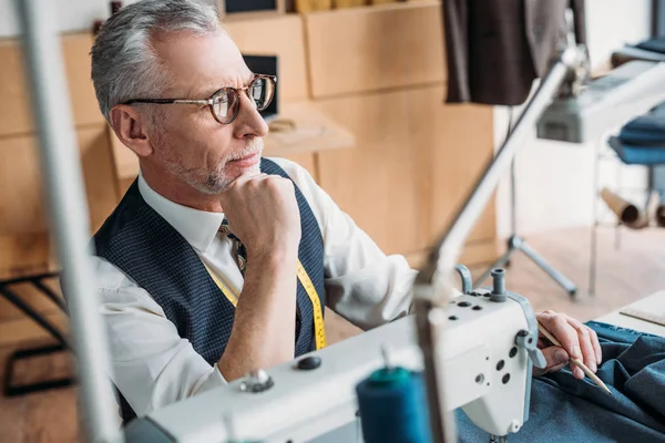 Pensive Tailor Sitting Table Sewing Machine Looking Away Sewing Workshop — Stock Photo, Image