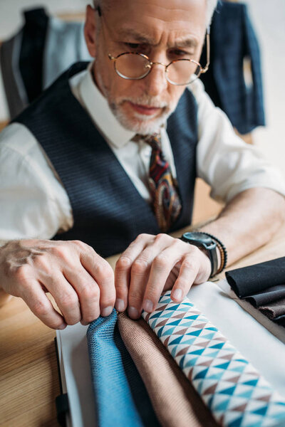 stylish mature tailor looking at cloth samples at sewing workshop