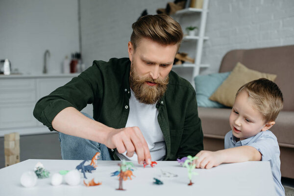 father and cute little son playing with various toy dinosaurs together at home