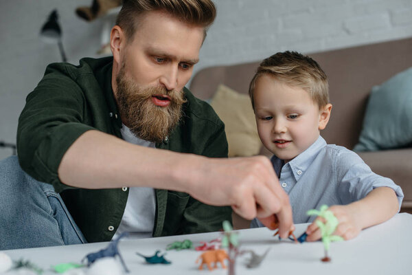 father and cute little son playing with various toy dinosaurs together at home