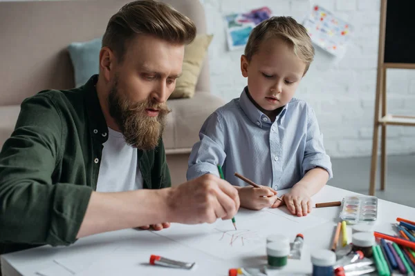 father and cute little son with colorful pencils drawing pictures together at home