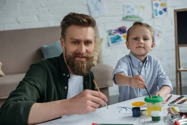 Sonriente Padre Lindo Hijo Pequeño Con Pinturas Pinceles Mirando Cámara — Foto de Stock